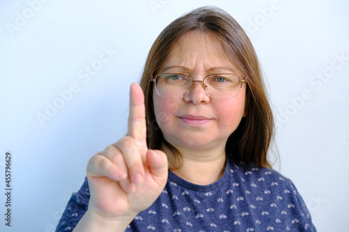 displeased  angry adult woman 40-49 years old in headphones speaks  talks  points a finger on a light background  blog post concept  blogger s lifestyle