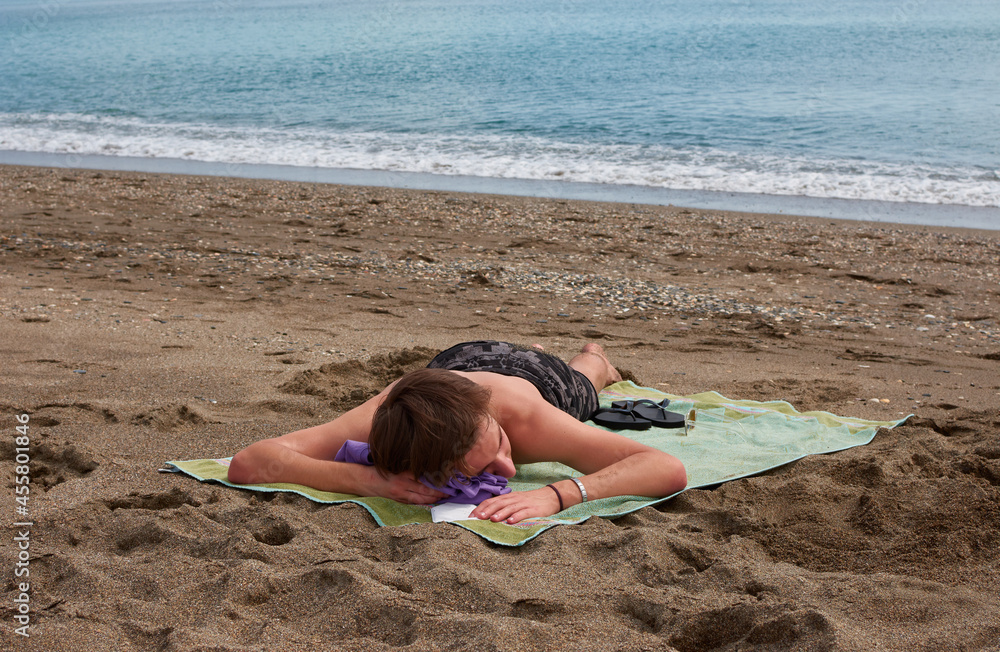 A young Caucasian male laying on a towel on a beach A young Caucasian male laying on a towel on a beach