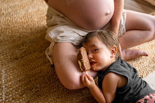 Funny boy with ice cream lying on his pregnant mom photo