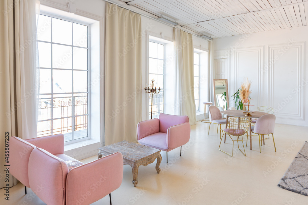 Fototapeta premium delicate and cozy light interior of the living room with modern stylish furniture of pastel pink color and white walls with stucco moldings in daylight