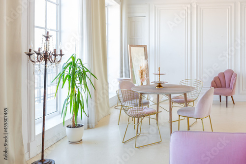 delicate and cozy light interior of the living room with modern stylish furniture of pastel pink color and white walls with stucco moldings in daylight