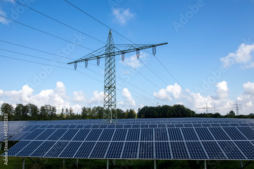 Renewable energy, electricity pylons in the middle of a large field of solar panels on a sunny day and blue sky