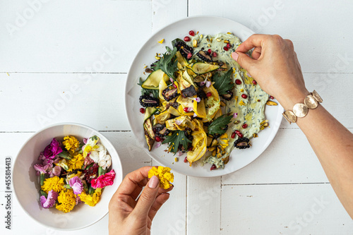 Hands plating a beautiful salad with side dish of edible flowers photo