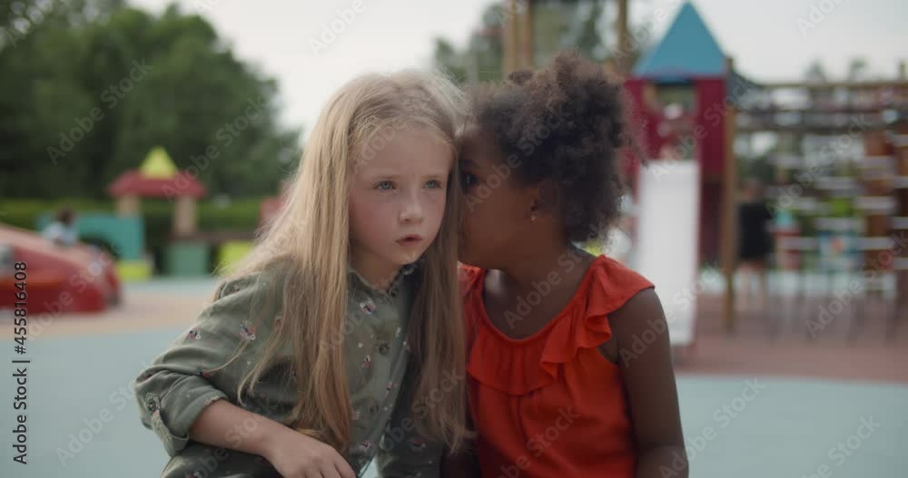Medium shot of multiracial little children tell secrets on bench outdoors Medium shot of multiracial little children tell secrets on bench outdoors
