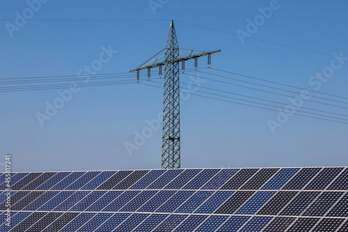 Renewable energy, electricity pylons in the middle of a large field of solar panels on a sunny day and blue sky