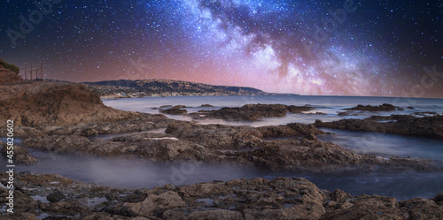 Milky way shimmers over the ocean water as it cascades over rocks