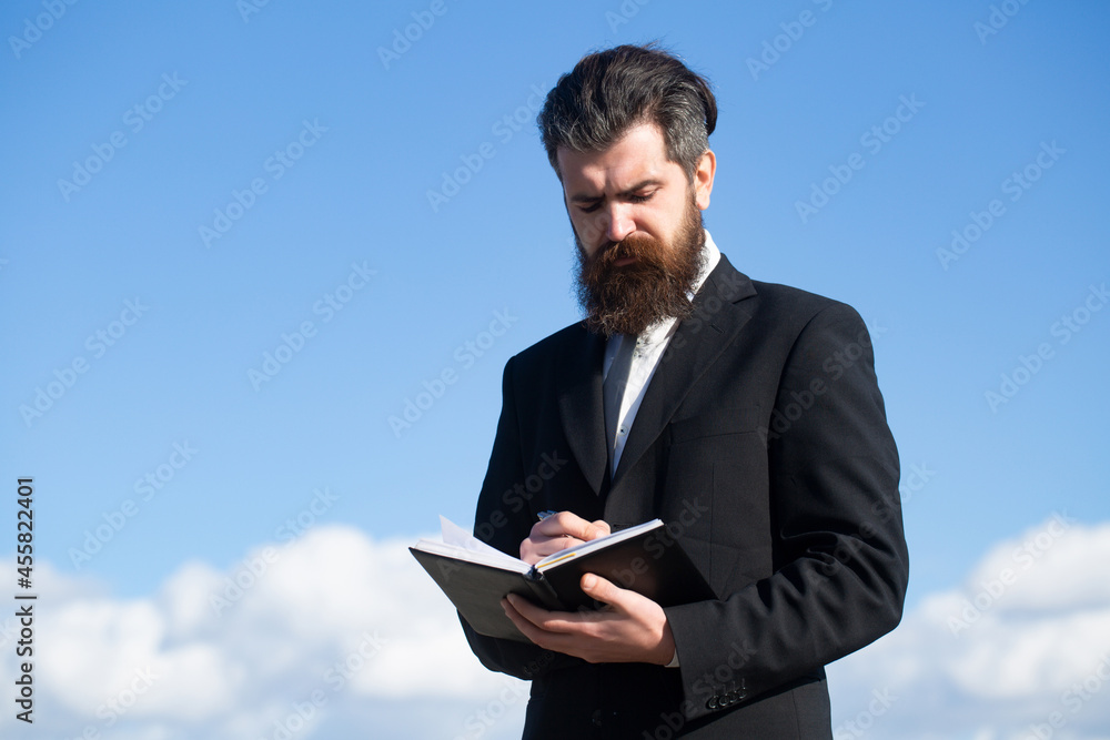 Business man with sky. Portrait with copy space of serious man holding copybook and with pen with thoughtful expression over sky background. Business man with sky. Portrait with copy space of serious man holding copybook and with pen with thoughtful expression over sky background.