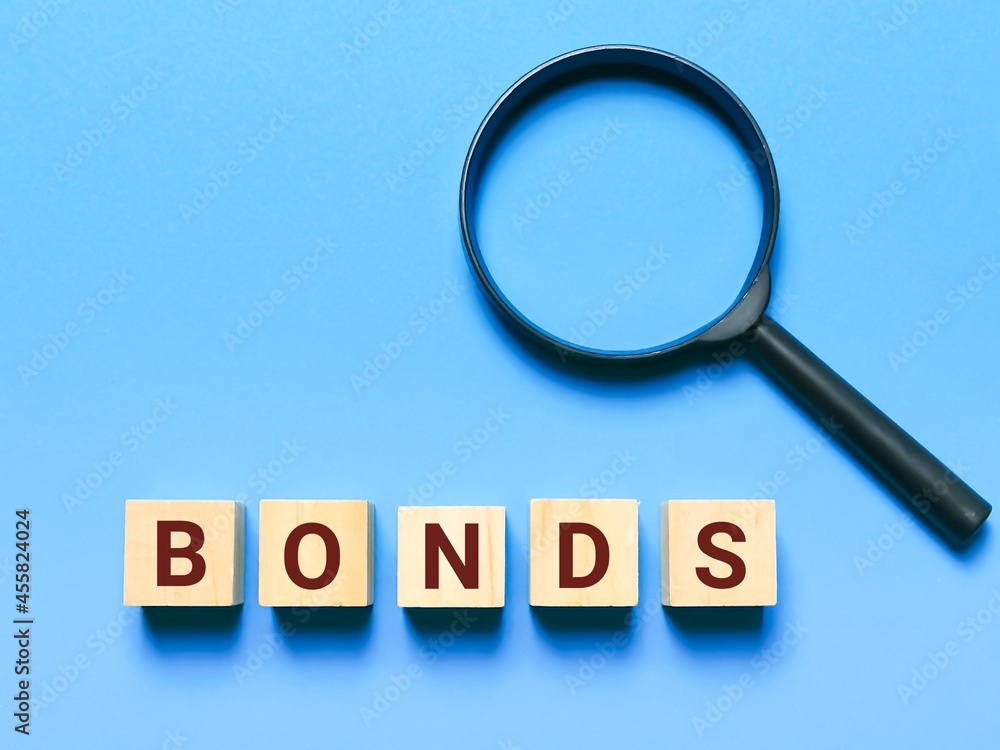Text bonds on wooden cubes with magnifying glass. Concept of assessment of value and investment. Text bonds on wooden cubes with magnifying glass. Concept of assessment of value and investment.