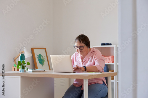 Glad woman with Down syndrome browsing laptop photo