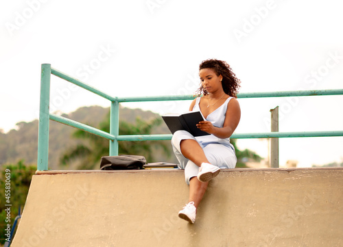 Young black woman reading a book in the public square.