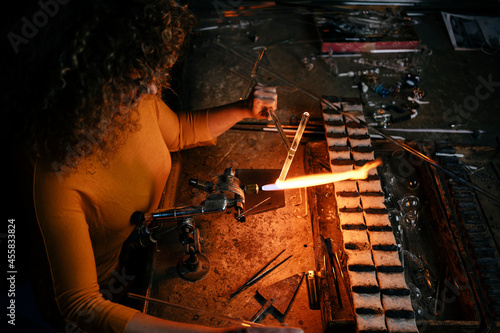 High angle view of woman lampworker working with glass tubes with the torch flame photo