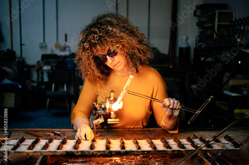 Front view of woman lampworker working with glass tubes with the torch flame photo