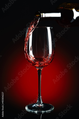 Pouring of red wine into glass on dark background