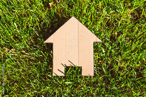 green home, house icon on green grass lawn under warm summer sunlight