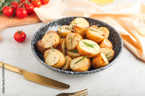 Plate with baked potatoes and rosemary on light background