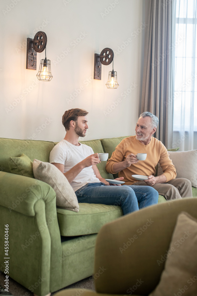 Two men sitting on the sofa and having tea