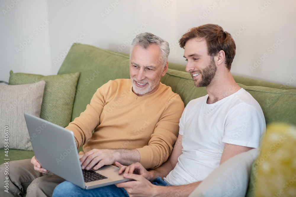 Young man and his dad watching something online and looking involved Young man and his dad watching something online and looking involved