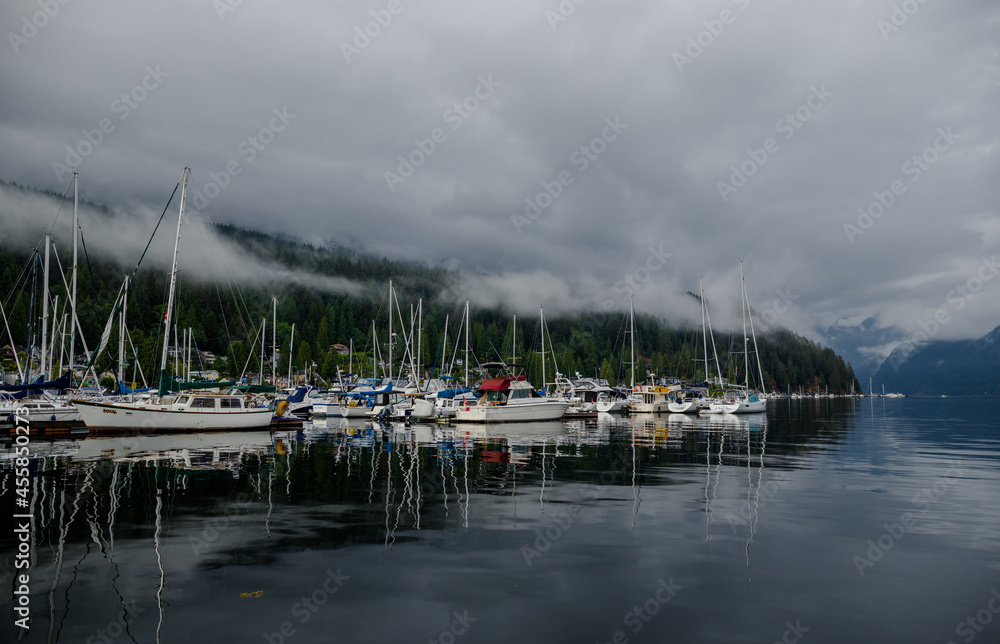 Sail, yachts and motor boats anchor in the  harbor. Calm water and the green misty mountains after rain. Deep Cove, British Columbia, Canada