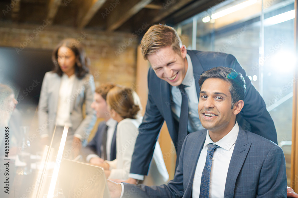 Businessmen smiling at laptop in conference room meeting Businessmen smiling at laptop in conference room meeting