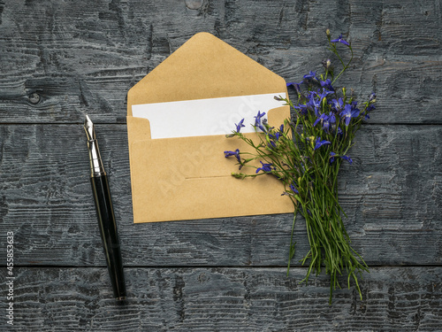 An open postal envelope with a sheet of paper, a fountain pen and a bouquet of flowers on a wooden table. Flat lay.