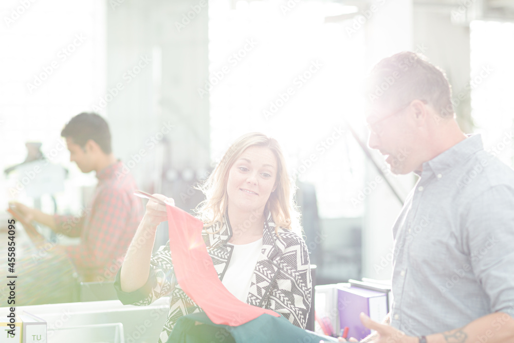 Fototapeta premium Fashion designers discussing fabric swatch in sunny office