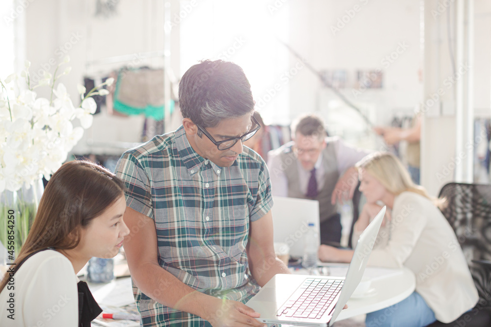 Smiling fashion designers working at laptop in office Smiling fashion designers working at laptop in office