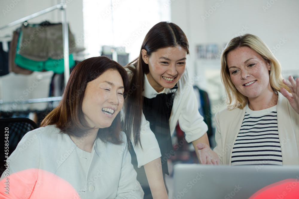 Smiling fashion designers working at laptop in office Smiling fashion designers working at laptop in office