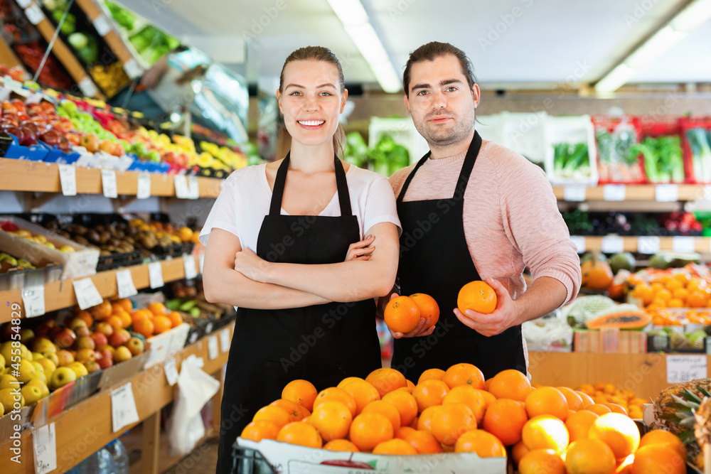 Young happy cheerful positive smiling man and woman wearing aprons holding fresh oranges on the supermarket