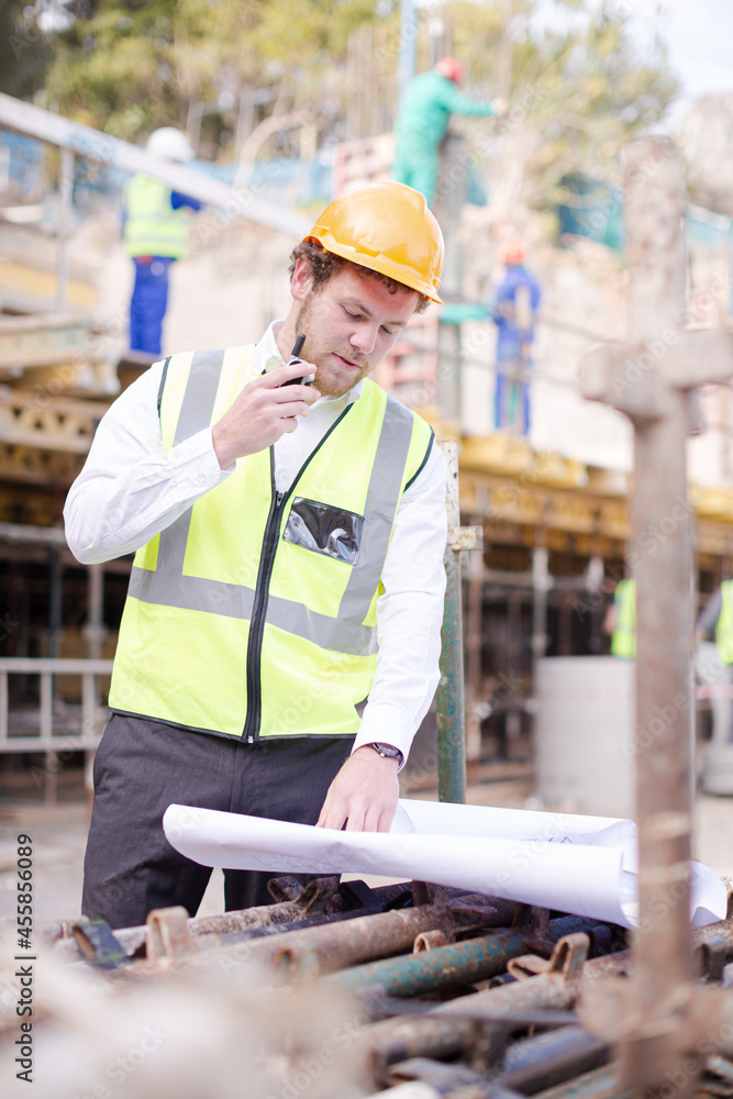 Engineer with blueprints walkie-talkie working at construction site Engineer with blueprints walkie-talkie working at construction site