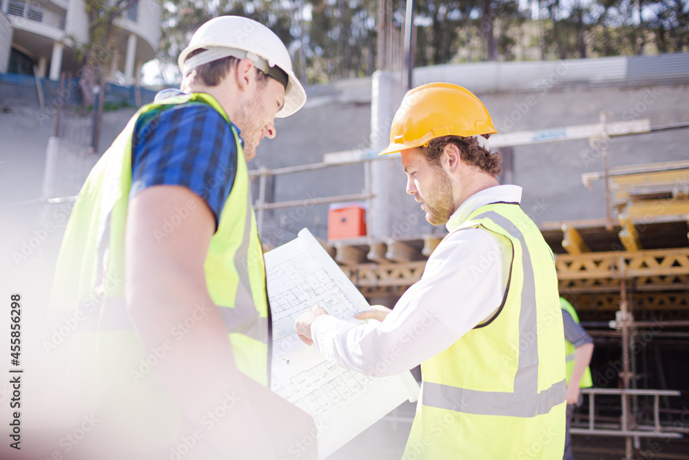 Construction worker engineer reviewing blueprints below crane at construction site Construction worker engineer reviewing blueprints below crane at construction site