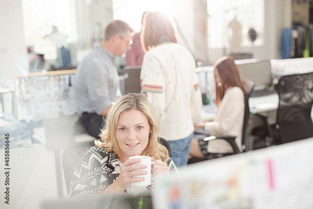 Fototapeta premium Portrait smiling fashion designer drinking coffee at computer in office