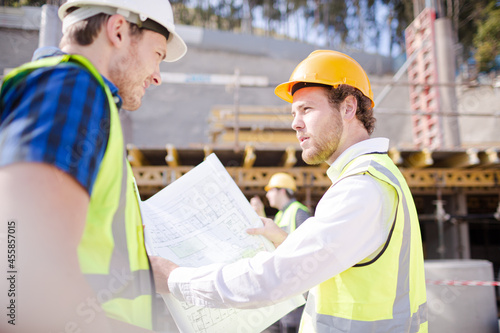 Construction worker engineer reviewing blueprints below crane at construction site