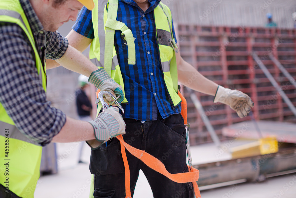 Construction worker fastening coworker’s safety harness Construction worker fastening coworker’s safety harness