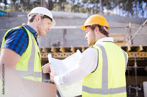 Construction worker engineer reviewing blueprints below crane at construction site