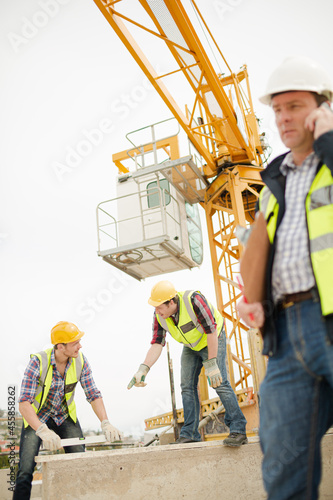 Construction workers using level tool below crane at construction site