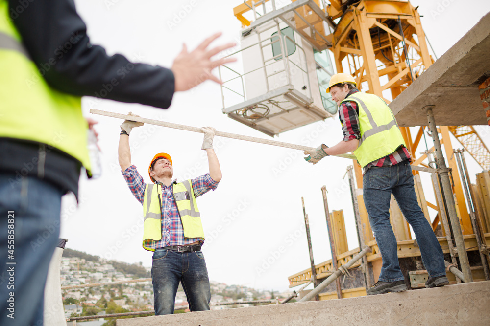 Construction workers lifting metal pole below crane at construction site Construction workers lifting metal pole below crane at construction site