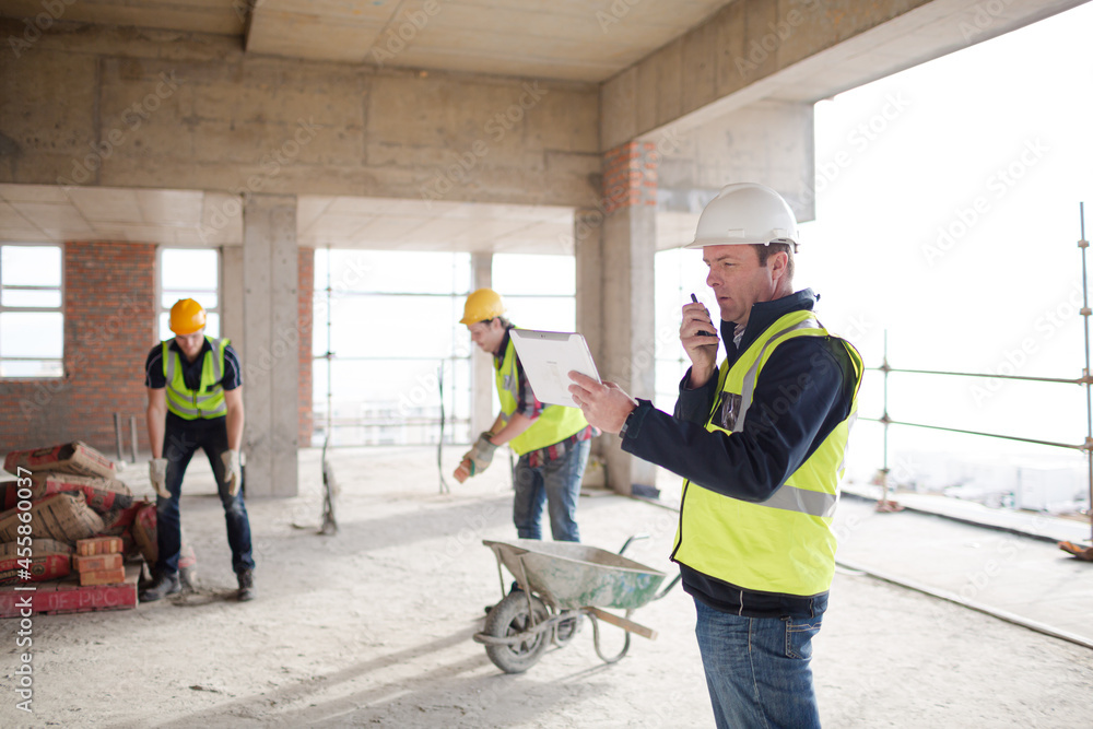 Foreman with digital tablet using walkie-talkie at construction site Foreman with digital tablet using walkie-talkie at construction site