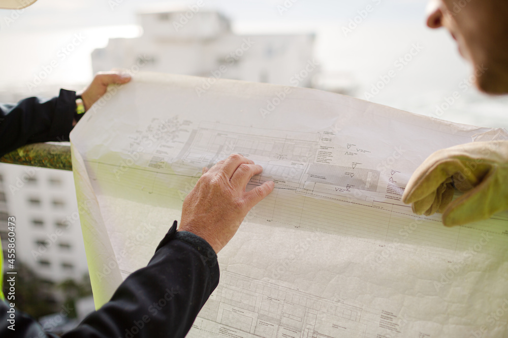 Naklejka premium Construction worker engineer reviewing blueprints at highrise construction site