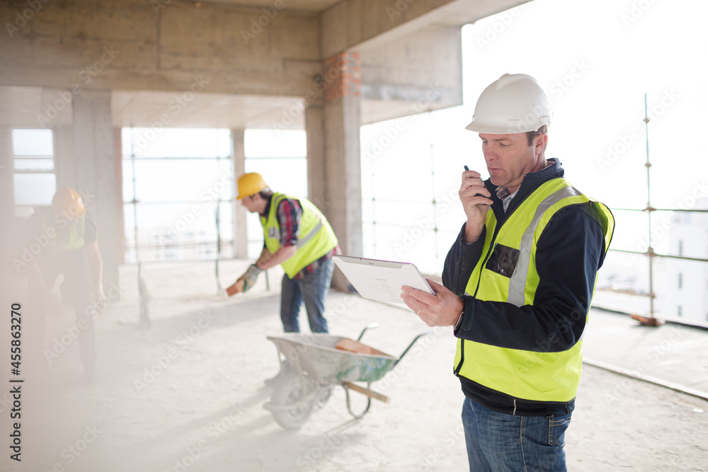 Foreman with digital tablet using walkie-talkie at construction site Foreman with digital tablet using walkie-talkie at construction site