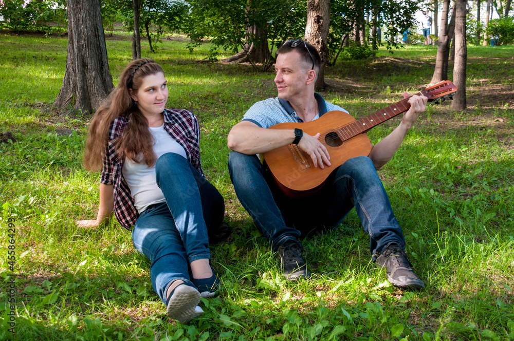 Young couple on the grass in the park in the summer, a guy plays the guitar for a girl