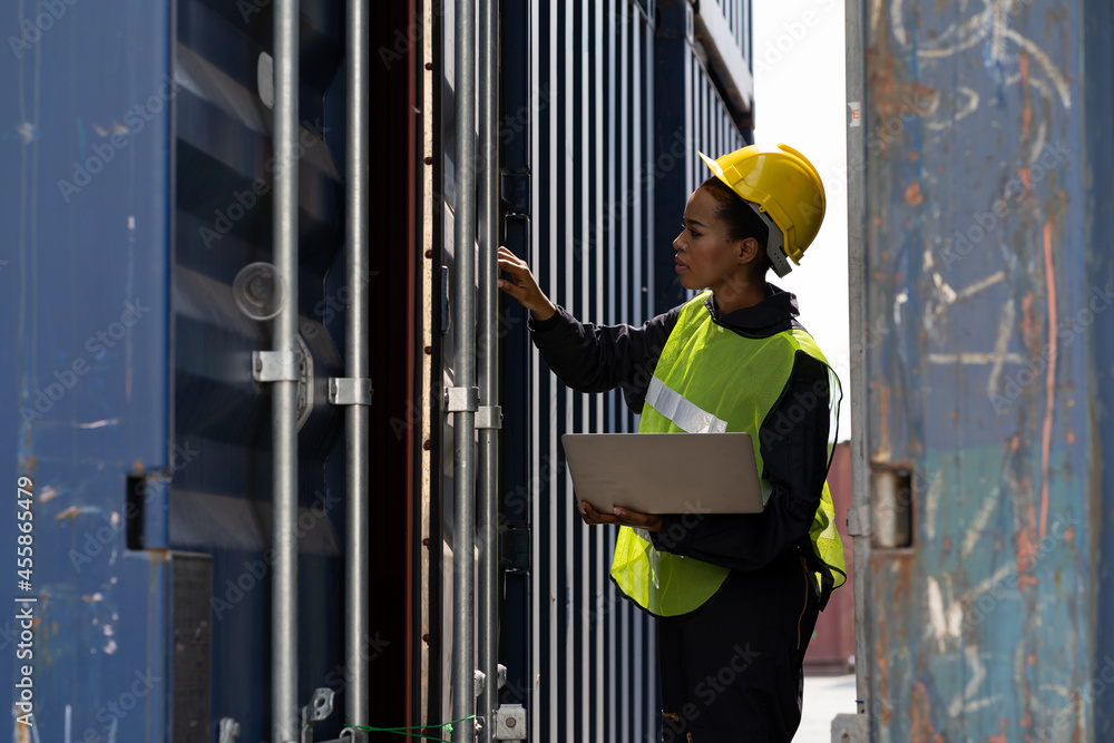 Female technician worker working at the commercial dock. African American female worker using computer laptop checking quality of steel container box from cargo freight at commercial dock site Female technician worker working at the commercial dock. African American female worker using computer laptop checking quality of steel container box from cargo freight at commercial dock site