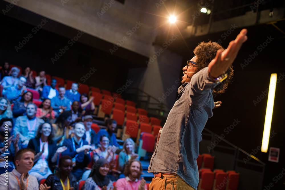 Audience watching male speaker with arms outstretched on stage