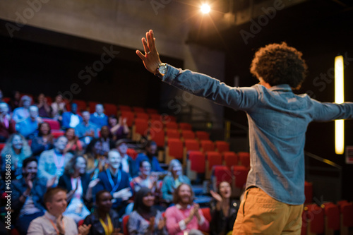 Audience watching male speaker with arms outstretched on stage