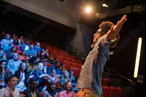 Audience watching male speaker with arms outstretched on stage © KOTO