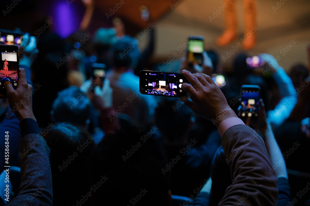Audience members with smart phones videoing speaker on stage at conference Audience members with smart phones videoing speaker on stage at conference