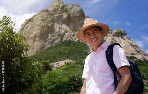 Smiling latin tourist with hat and backpack, on a mountain. Smiling man in Peña de Bernal traveling. Vacation concept
