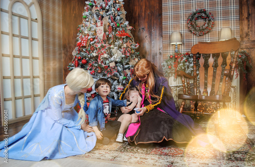 kids with the main characters of Disney Elsa and Anna cold heart waiting for Santa Claus for the New Year and Christmas at home against the background of the tree