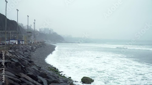 Static shot of a foggy morning off the coast of Roquitas, Malecon de Miraflores, Lima, Peru with waves at a rocky beach photo