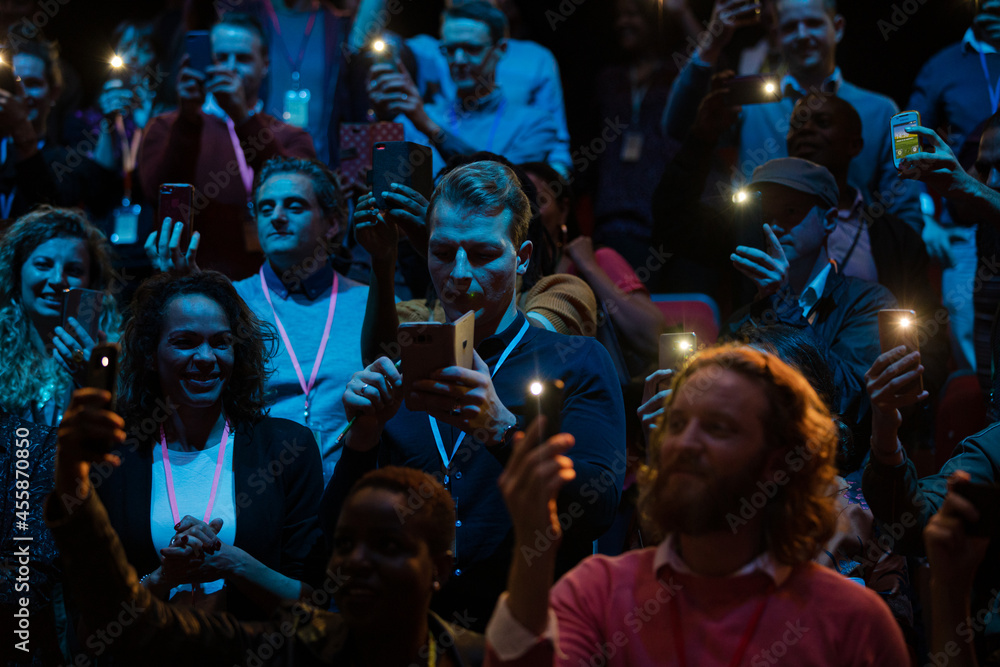 Fototapeta premium Smiling audience using smart phone flashlights for speaker