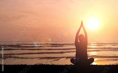 Silhouette of young woman practicing yoga on meadow beach at sunset.
